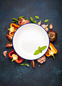 Empty plate surrounded by a selection of vegetables and basil