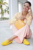 Long-haired young woman with braid in striped blouse and pink trousers, yellow shoes