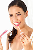 Young woman applying make-up with lip gloss