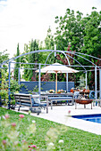 Sitzbereich mit Holzbank und Feuerstelle am Pool im Garten
