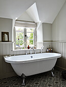 Free-standing bathtub in front of transom window in bathroom with patterned tiled floor