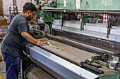 A worker operating a large powerloom weaving machine at Hilandería Warmi, a weaving mill in Palpalá, Argentina.