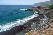 A scenic view of Playa del Bollullo on the north coast of Tenerife in La Orotava, showcasing black sand, blue ocean, and beachgoers.