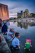 Children float a candle-lit lantern on a river, in front of Atomic Bomb Dome with floating lamps on Motoyasu-gawa River during Peace Memorial Ceremony every August 6 in Hiroshima, Japan