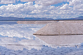 Salt mining operations on the salt flats of Salinas Grandes in northwest Argentina. Clouds are reflected on a shallow sheet of water.