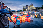 Woman float lanterns on the river, in front of Atomic Bomb Dome with floating lamps on Motoyasu-gawa River during Peace Memorial Ceremony every August 6 in Hiroshima, Japan