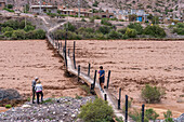 Tourists on a footbrideg over the flooding Rio Grande near Purmamarca after heavy rains in the Quebrada de Humahuaca in Argentina.