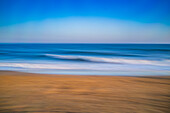 A calming long exposure photograph capturing the gentle waves of the ocean during a beautiful sunset on a sandy beach.