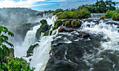 Iguazu Falls National Park in Argentina. A UNESCO World Heritage Site. Pictured is the precipice of Mbigua Falls and San Martin Falls with a stone arch or window in the background at the end of the falls.