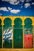 Lebendige und farbenfrohe Wand einer mobilen Stierkampfarena in Aznalcazar, Sevilla, unter strahlend blauem Himmel. Mit Graffiti und architektonischen Details