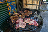 Meat cooking over coals in a wood-fired grill in the outdoor kitchen of a parrilla in Caminito, La Boca, Buenos Aires, Argentina.