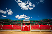 A scenic view of an empty portable bullring in Aznalcazar, Sevilla, Spain, showcasing vibrant colors under a clear blue sky.