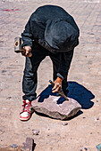 A stone mason shapes a stone with a hammer and chisel at a construction project in Tilcara, Argentina.