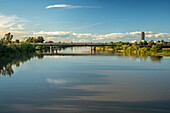 Peaceful view of Guadalquivir River flowing through Sevilla, Andalucia. Bridge and lush greenery under a clear blue sky create a serene landscape.