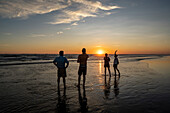 Sunset on the beach in Las Lajas, Panama. People stand on the beach silhouetted.