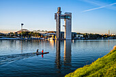 Beautiful riverside scene in Sevilla, Spain featuring two canoeists paddling near a modern tower against a clear blue sky.