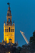 Atemberaubende Nachtansicht von La Giralda und dem Alamillo-Brückenmast in Sevilla, Spanien, aufgenommen mit einem Teleobjektiv. Die ikonische Architektur ist wunderschön beleuchtet