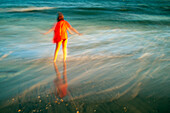 A vibrant long exposure photo of a girl in a red dress playing at the beach, capturing the motion of ocean waves.