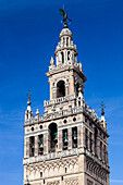 The Giralda tower stands majestically, showcasing its intricate architecture against a brilliant blue sky in Seville, Spain.