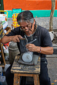 An artisan embossing a metal cup to sell to tourists on Magallanes Street in Caminito, La Boca, Buenos Aires, Argentina.