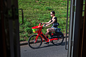 Young woman riding Lime rental bike in Prague, viewed from tram door