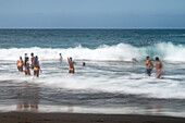 A group of bathers enjoying the waves at Bollullo Beach on the northern coast of Tenerife, La Orotava, Canary Islands, Spain. Long exposure.