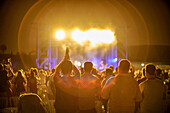 Vibrant rock concert scene with an enthusiastic crowd and bright stage lights, uniquely captured through a vintage lens creating an atmospheric and nostalgic effect.