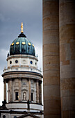 Columns of the Konzerthaus stand tall, highlighting the German Cathedral in Gendarmenmarkt, Berlin under a dramatic sky.