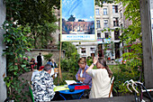 Guests gather at a cozy open-air restaurant in Mitte, Berlin, savoring food and conversation amidst lush greenery on a summer evening.