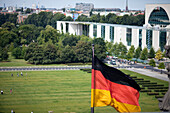 The panoramic view captures the German Chancellery beside the Reichstag with the German flag waving prominently in the foreground.