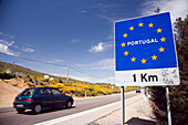 Travelers drive towards the Portugal border, marked by a prominent sign, in the scenic region of Extremadura.