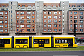 A yellow tram travels along Karl-Liebknecht street, showcasing urban life in Berlin\'s Mitte district beside residential buildings.