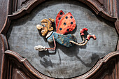 Caricature carved in wood of fairy godmother with legs and ladybug wings adorns a door in Prague.