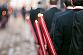 Members of a brotherhood participate in the Corpus Christi procession in Seville, carrying lit candles along a cobbled street.