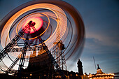 The Ferris wheel at Tibidabo amusement park spins against a sunset backdrop, illuminating the sky with vibrant lights.