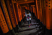 Young caucasian woman exploring Fushimi Inari Taisha temple at night, Kyoto, Japan