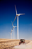 Windmills generate electricity while a tractor cultivates land in Sanlucar de Barrameda, showcasing renewable energy in action.