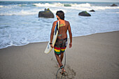 Surfer entering the sea on the beach in front of Finca Barlovento, Tayrona National Park, Colombia