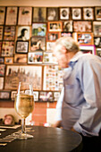 An old tavern in Spain features a patron walking by, while a drink rests on the table, surrounded by nostalgic photographs.