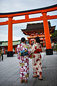 Two young women wearing traditional Japanese clothes and the torii gate of Fushimi Inari, Kyoto, Japan