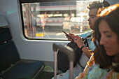 Travelers using smartphone in train to airport at sunset, Madrid