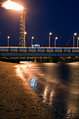 Flames and lights illuminate the facilities of a regasification plant along the coast at nighttime in Huelva, Andalusia.