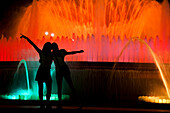 Visitors enjoy the vibrant light show of the Montjuic fountain, surrounded by colorful water jets in Barcelona’s night.