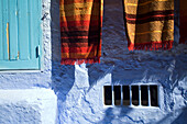 Colorful carpets hang outside shops in the vibrant town of Chefchaouen, showcasing local craftsmanship and culture.