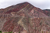 Niedrige Wolken über den gestreiften Felsschichten eines Berges auf der anderen Seite des Flusses bei Purmamarca, Argentinien