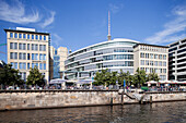 Contemporary buildings stand by the Spree river, offering views of iconic Berlin landmarks and vibrant riverside activity.