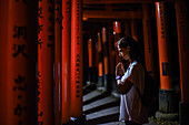 Young caucasian woman praying at Fushimi Inari Taisha temple at night, Kyoto, Japan