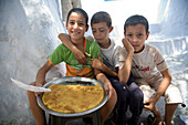 Chefchaouen, Morocco, July 3 2007, Three children sit happily presenting their homemade cakes for sale in Chefchaouen, showcasing local entrepreneurial spirit in the afternoon.