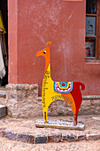 A sign in the shape of a llama in front of a colorfully-painted souvenir shop in Purmamarca, Argentina.