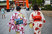 Two young women wearing traditional Japanese clothes and the torii gate of Fushimi Inari, Kyoto, Japan